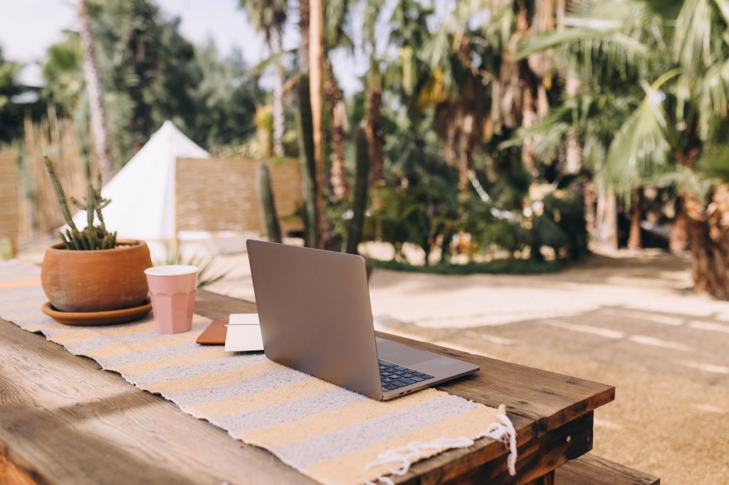 Laptop on an outdoor table surrounded by trees, capturing the calm balance of work and nature — the essence of a workation.
